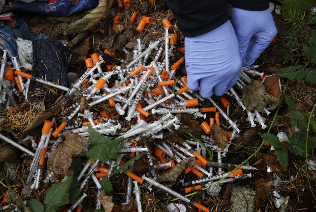 A volunteer cleans up needles used for drug injection that were found at a homeless encampment at Everett, Washington.