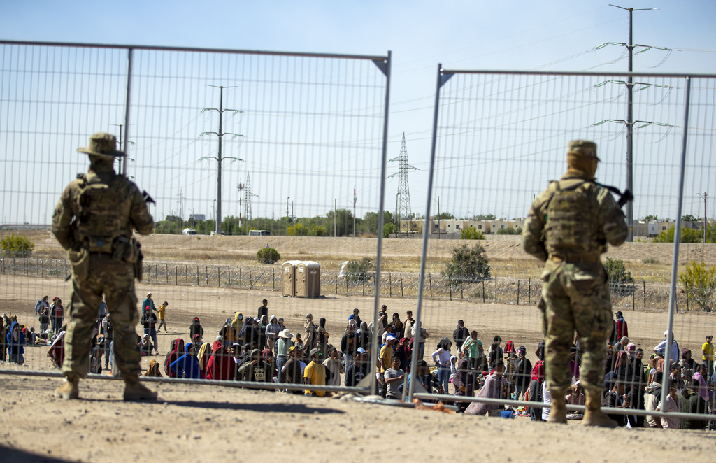 Migrants wait in line adjacent to the border fence under the watch of the Texas National Guard to enter into El Paso, Texas.