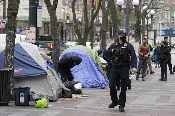 A Seattle police officer walks past tents during the clearing and removal of a homeless encampment in Westlake Park at downtown Seattle, March 11, 2022.