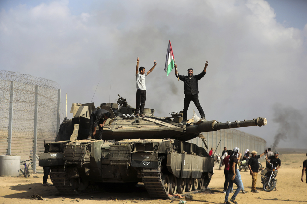 Palestinians wave their national flag and celebrate by a destroyed Israeli tank at the Gaza Strip fence east of Khan Younis, October 7, 2023.