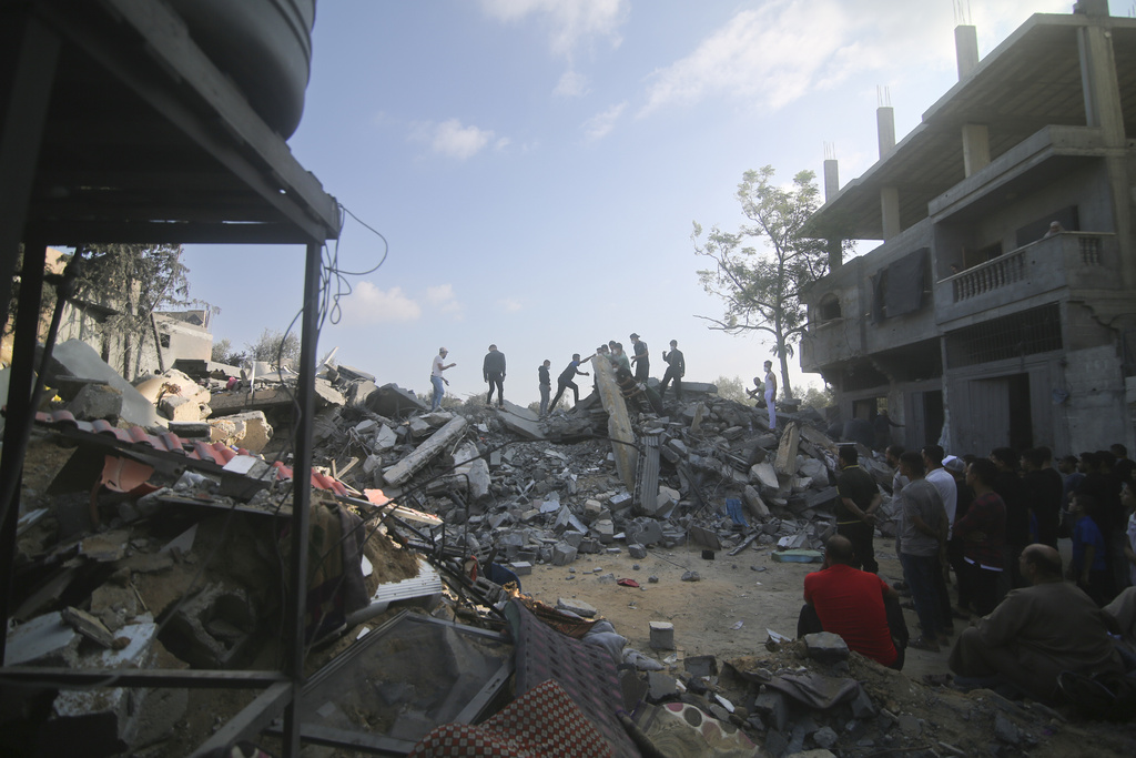 Palestinians stand by the building destroyed in an Israeli airstrike in Rafah, Gaza Strip, Saturday, Oct. 14, 2023.