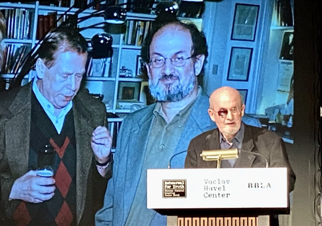 Novelist Salman Rushdie makes a surprise appearance at the Bohemian National Hall on Tuesday night to accept a literary freedom award from the Vaclav Havel Center. In the background is a photo of the British-American writer on a visit to Prague, with then-president Havel and his wife Dagmar Havlová.