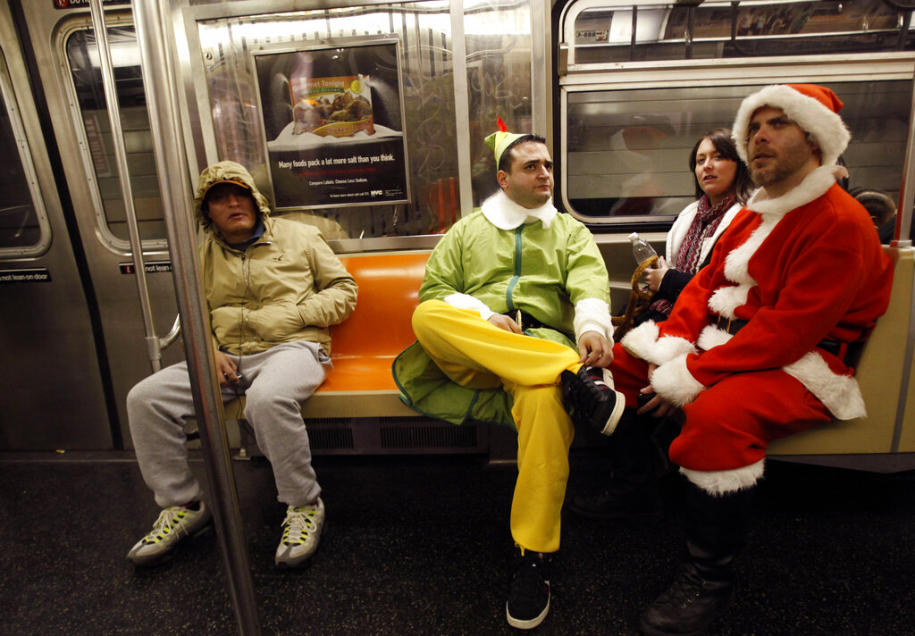 FILE- In this Dec. 11, 2010 file photo, SantaCon participants John Paul, center, dressed as an Elf and Michael Smallwood, dressed as Santa, ride the E train downtown New York. The annual event has faced mounting pressure from politicians, police and community groups as it grew from hundreds to thousands of costumed participants in roughly a decade. This years festivities fall on the same day as a planned march to protest recent killings of unarmed civilians by police. Santacon organizers are asking celebrants to keep their partying indoors