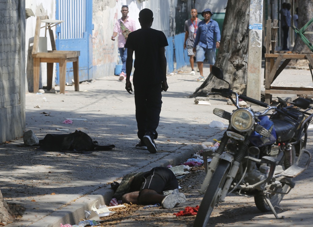 A lifeless body lies against the curb as pedestrians walk past at Port-au-Prince, Haiti, Monday, March 11, 2024.
