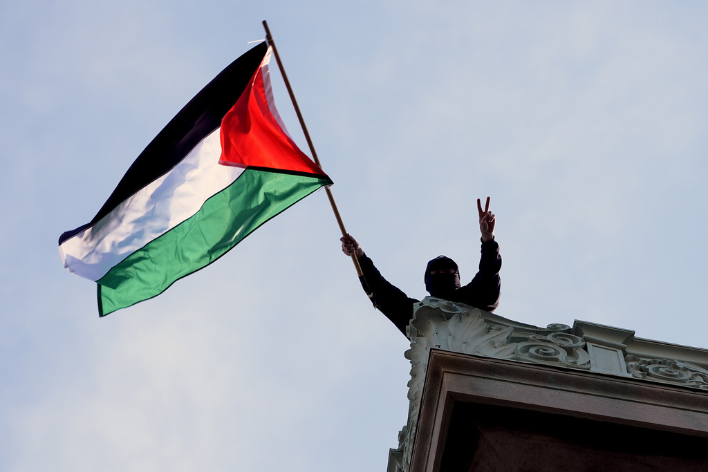 A student protester waves a Palestinian flag above Hamilton Hall on the campus of Columbia University, Tuesday, April 30, 2024, in New York. Early Tuesday, dozens of protesters took over Hamilton Hall, locking arms and carrying furniture and metal barricades to the building. Columbia responded by restricting access to campus.