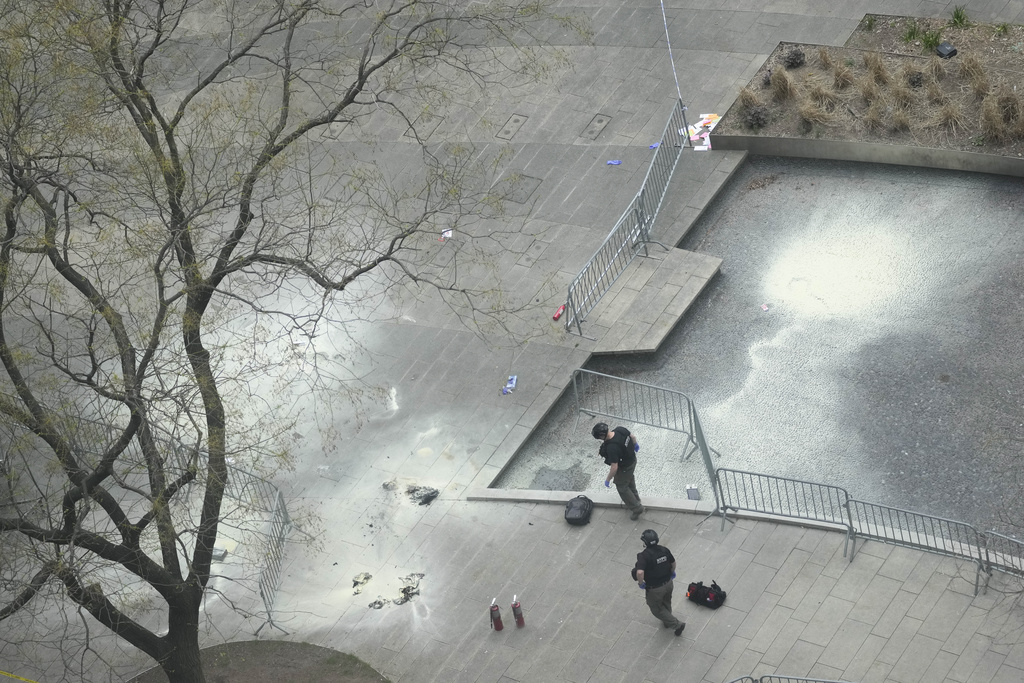 New York Police officers inspect a backpack left at the scene where a man lit himself on fire in a park outside Manhattan criminal court, Friday, April 19, 2024, at New York.