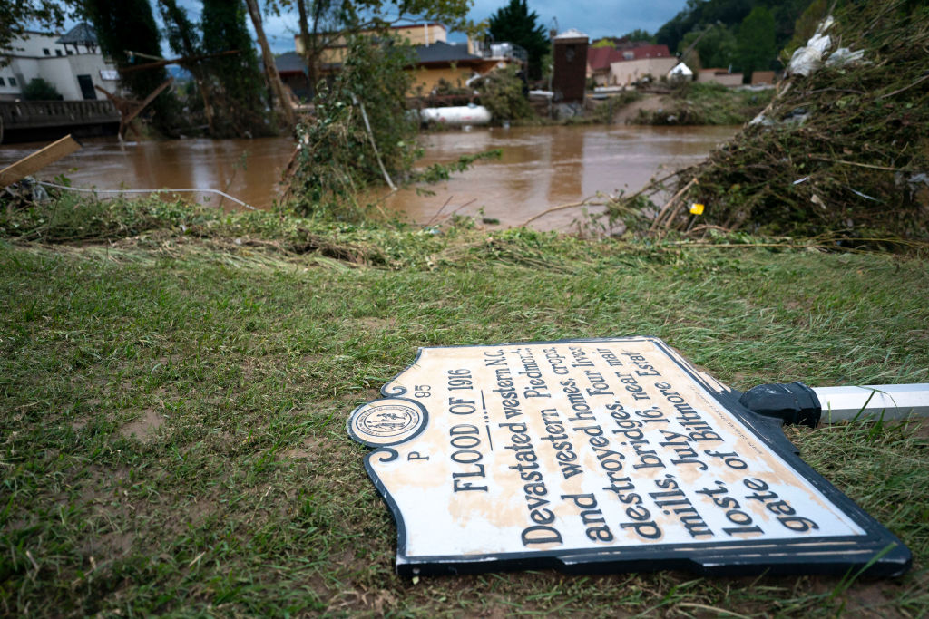 A sign commemorating the flood of 1916 lies on the ground next to a flooded waterway near the Biltmore Village in the aftermath of Hurricane Helene on September 28, 2024 at Asheville, North Carolina.