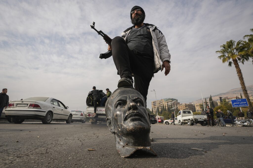 An opposition fighter steps on a broken bust of the late Syrian President Hafez Assad in Damascus, Syria, Sunday Dec. 8, 2024.