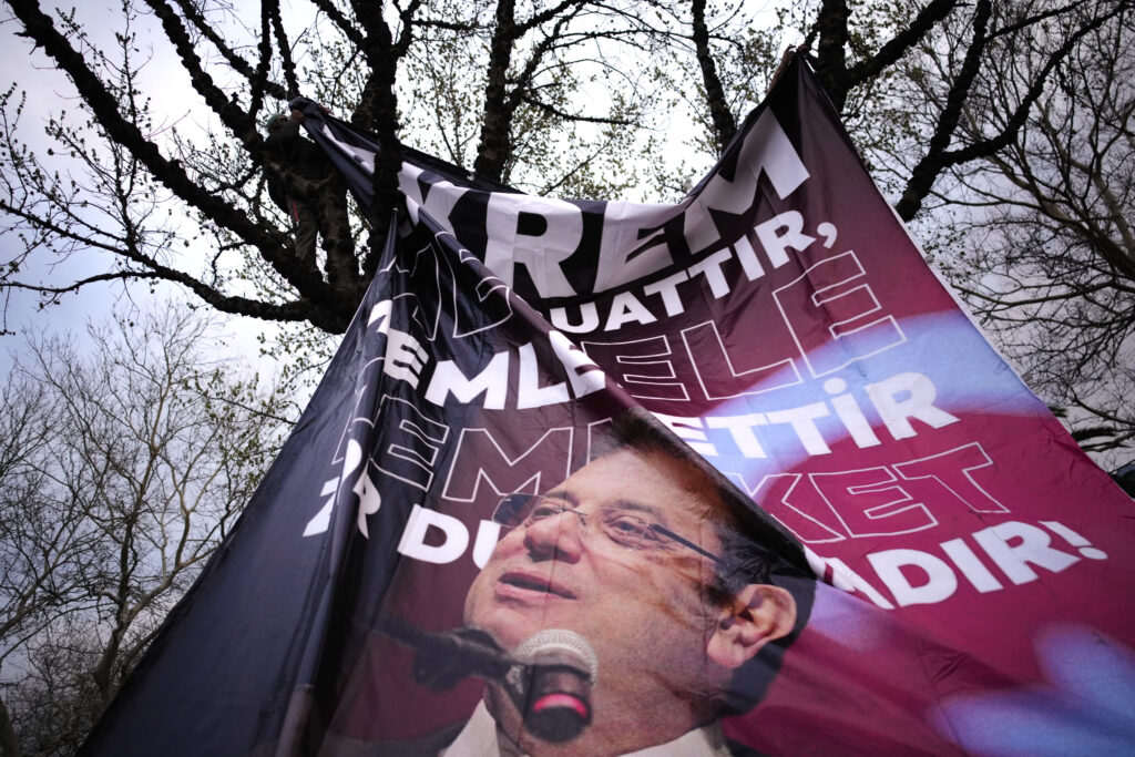 A man attaches a large banner of Istanbul's Mayor Ekrem Imamoglu in a tree in Istanbul, Turkey on March 20, 2025, during a protest against the arrest of Mr. Imamoglu on corruption charges.