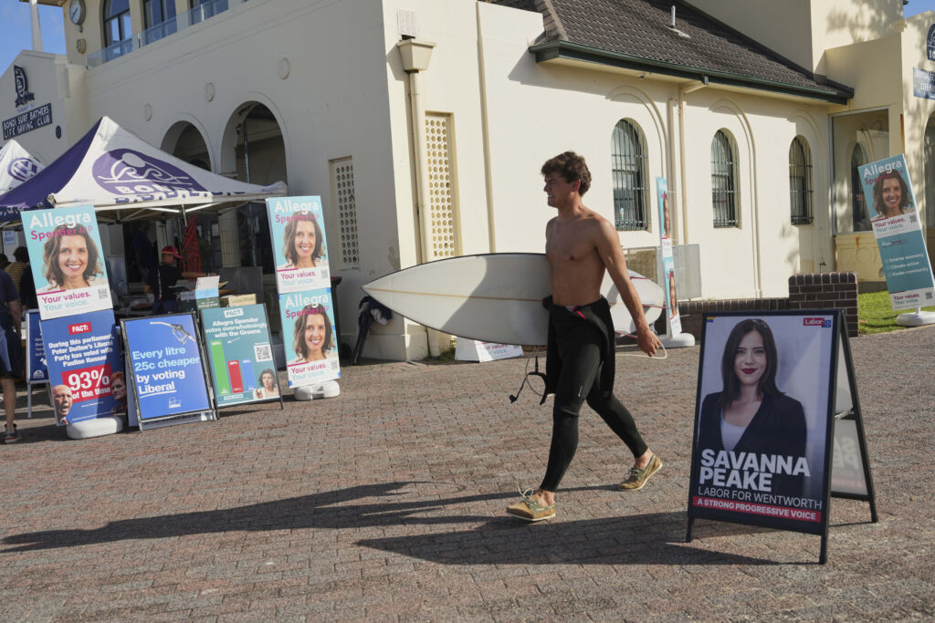 A surfer carries his board as he walks past a polling booth at Sydney's Bondi Beach, Saturday, May 3, 2025.