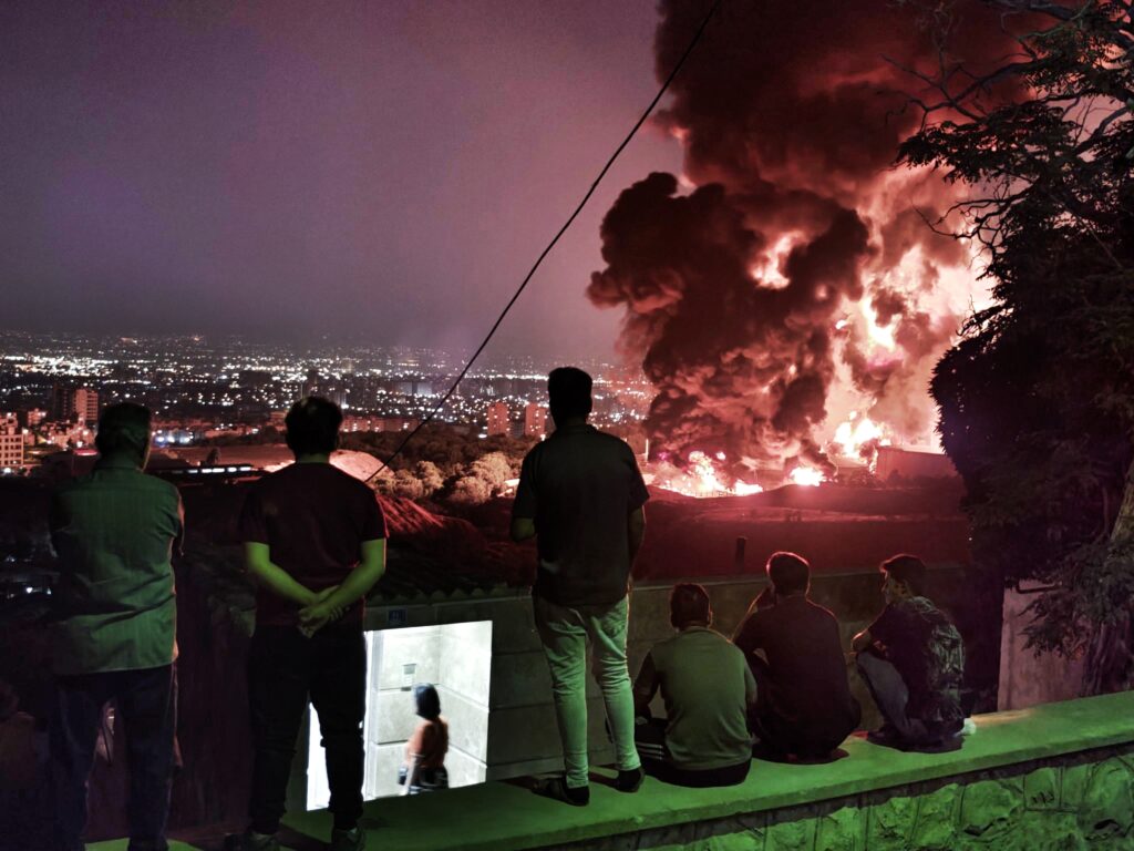 People observe fire and smoke from an Israeli attack on the Shahran oil depot on June 15, 2025 in Tehran, Iran. Iran's foreign minister said the country would respond "decisively and proportionally" to a wave of attacks that Israel launched beginning in the early hours of June 13. The attacks targeted multiple military, scientific and residential locations, as well as senior government officials.