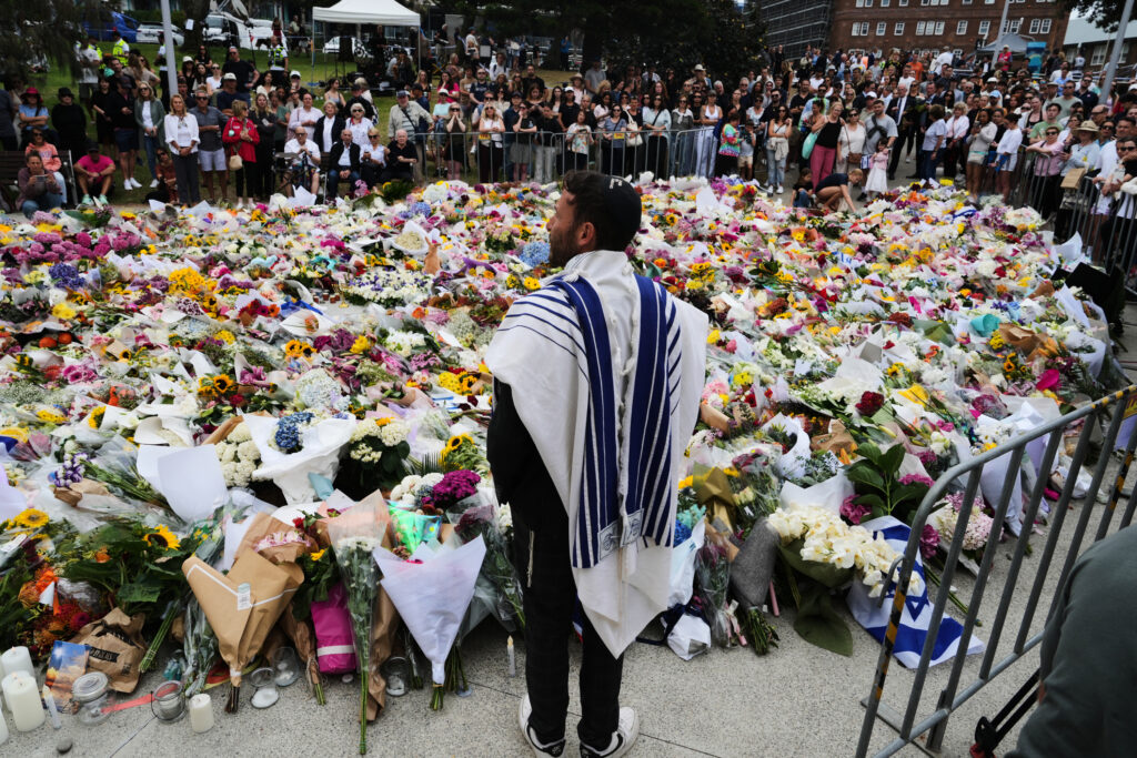 Rabbi Yossi Friedman speaks to people gathering at a flower memorial by the Bondi Pavilion at Bondi Beach on Tuesday.